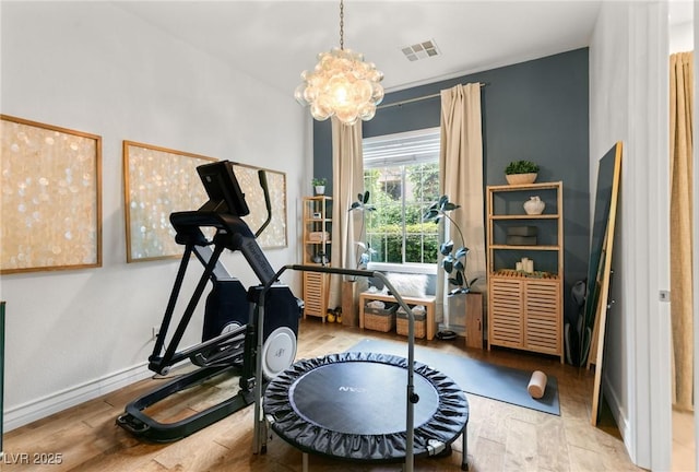 workout room featuring an inviting chandelier, wood finished floors, and visible vents