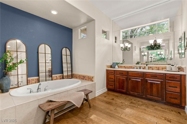 bathroom with an inviting chandelier, wood finished floors, a garden tub, and vanity