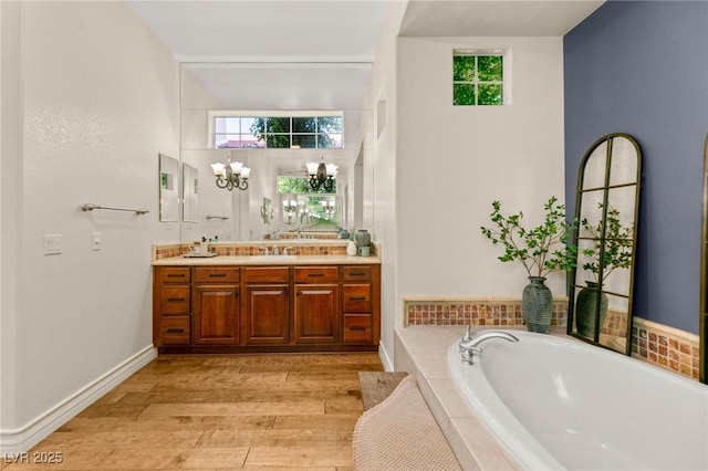 full bath featuring an inviting chandelier, double vanity, plenty of natural light, wood finished floors, and a garden tub