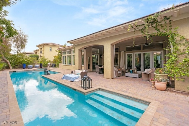 rear view of property featuring ceiling fan, a pool with connected hot tub, a patio, outdoor lounge area, and stucco siding