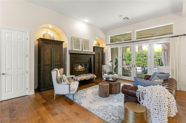 living room featuring visible vents, baseboards, a glass covered fireplace, and wood finished floors