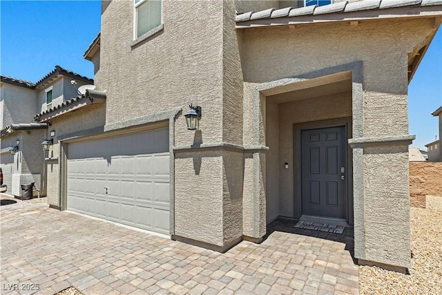 view of exterior entry featuring stucco siding, a garage, and decorative driveway
