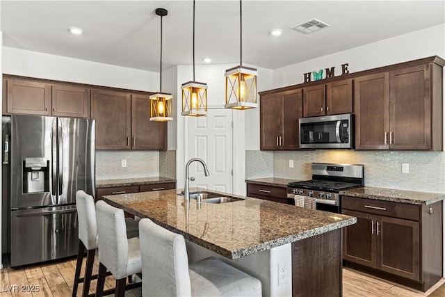 kitchen featuring stainless steel appliances, a sink, dark brown cabinetry, light wood-type flooring, and recessed lighting