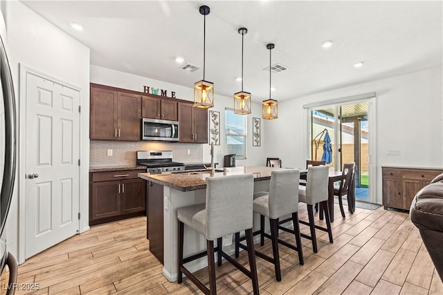 kitchen featuring appliances with stainless steel finishes, light wood-type flooring, dark brown cabinets, a kitchen breakfast bar, and tasteful backsplash