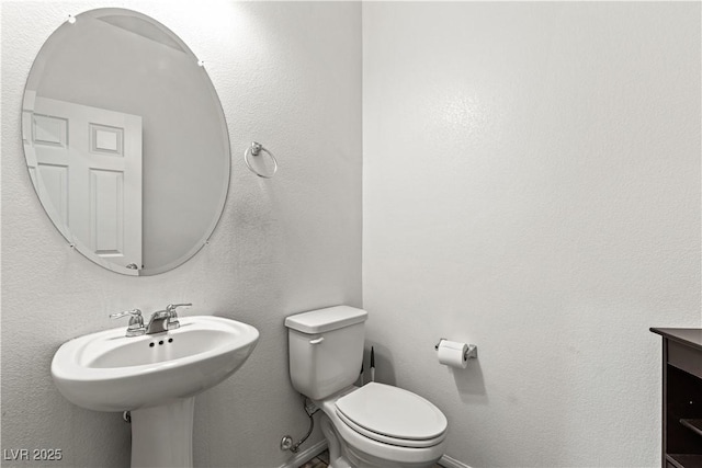 half bath featuring toilet, a sink, and baseboards