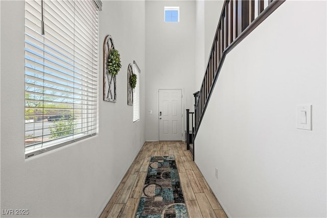 corridor featuring light wood-style floors, a towering ceiling, and stairs