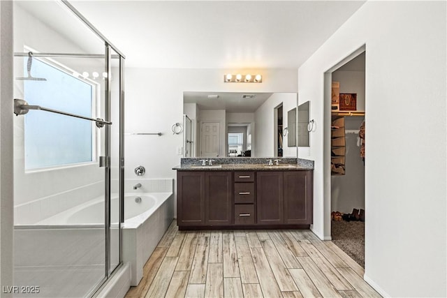 bathroom featuring a shower stall, a bath, double vanity, wood finished floors, and a walk in closet
