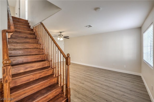staircase with a ceiling fan, baseboards, visible vents, and wood finished floors