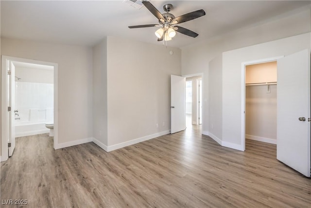 unfurnished bedroom featuring a closet, baseboards, light wood-type flooring, connected bathroom, and a spacious closet