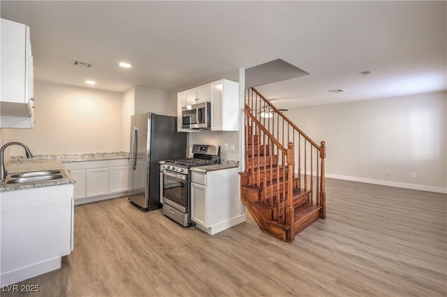 kitchen featuring appliances with stainless steel finishes, a sink, white cabinetry, baseboards, and light wood-type flooring