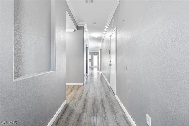 hallway featuring baseboards, ornamental molding, a textured wall, and wood finished floors