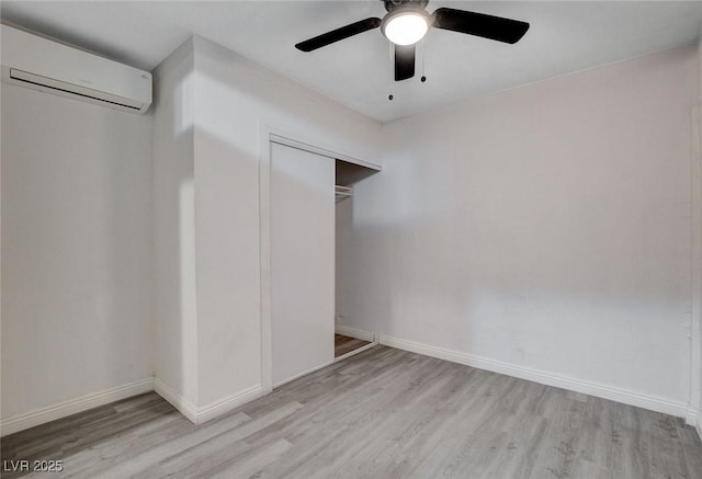 unfurnished bedroom featuring baseboards, a wall unit AC, wood finished floors, and a closet
