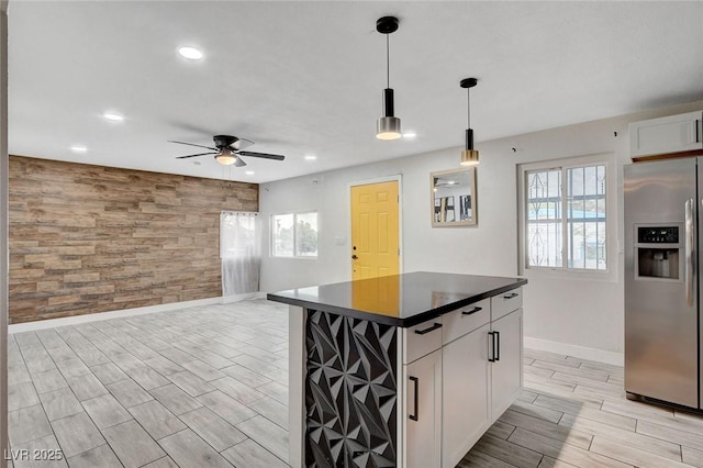 kitchen with an accent wall, dark countertops, baseboards, ceiling fan, and stainless steel fridge with ice dispenser