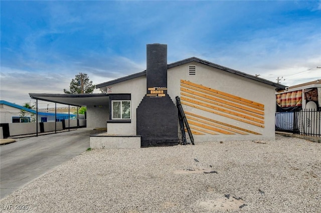 modern home featuring fence, stucco siding, a chimney, an attached carport, and driveway