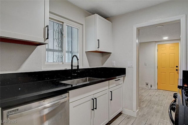 kitchen with white cabinets, dark countertops, a sink, and dishwasher