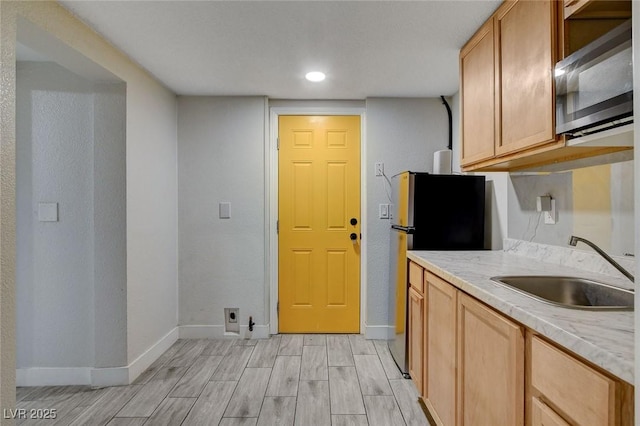 kitchen featuring freestanding refrigerator, baseboards, light wood-style floors, light countertops, and a sink