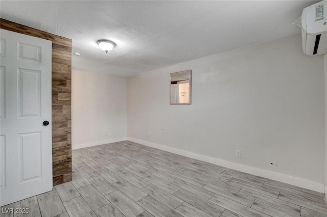 unfurnished room with an AC wall unit, wood finish floors, and baseboards