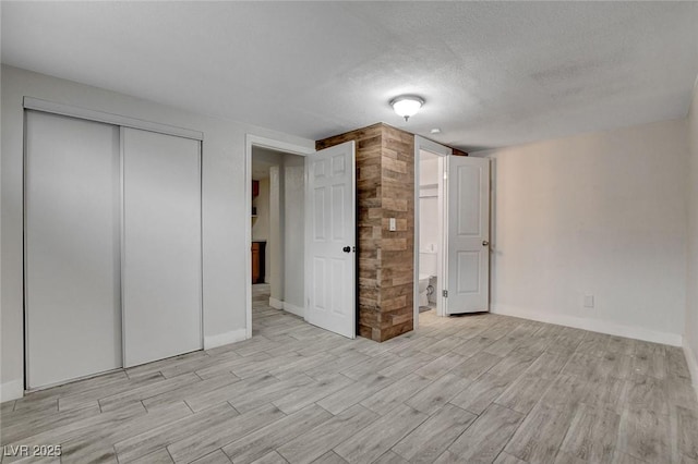 unfurnished bedroom featuring baseboards, a textured ceiling, light wood-style flooring, and a closet