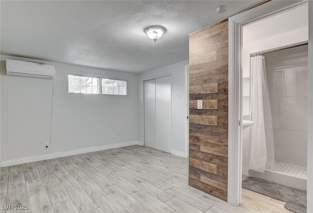 interior space with light wood-type flooring, a wall mounted air conditioner, a textured ceiling, and ensuite bath