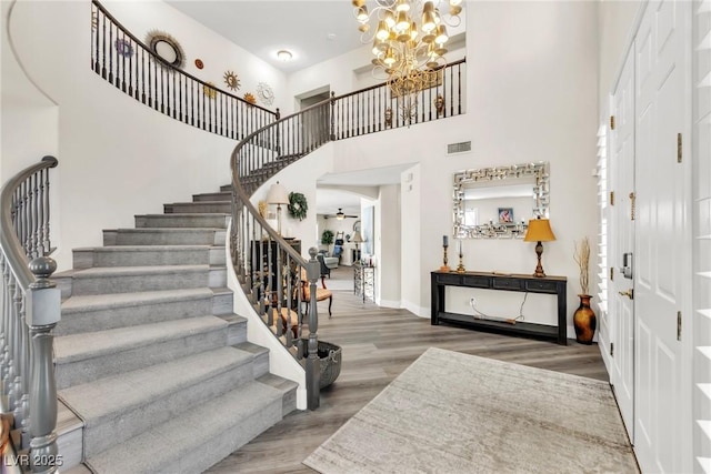 foyer featuring stairway, an inviting chandelier, wood finished floors, and visible vents