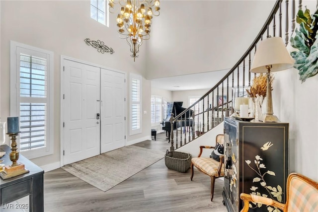 foyer entrance with wood finished floors, stairway, baseboards, an inviting chandelier, and a high ceiling