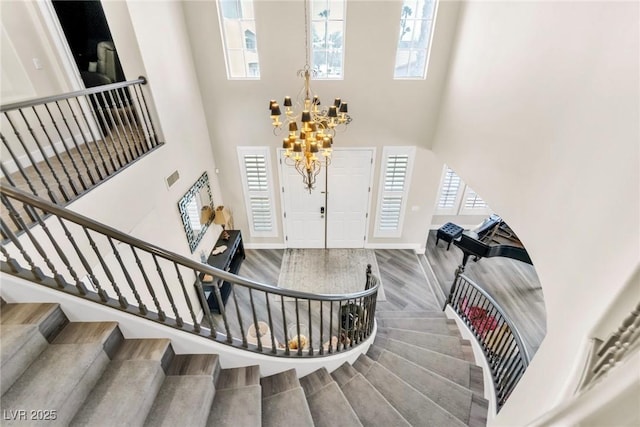 foyer with an inviting chandelier, a towering ceiling, wood finished floors, and stairway
