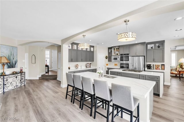 kitchen with a sink, appliances with stainless steel finishes, a kitchen island with sink, and gray cabinetry