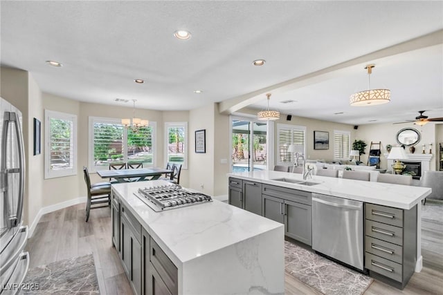 kitchen with gray cabinets, a center island with sink, a sink, light wood-style floors, and stainless steel appliances