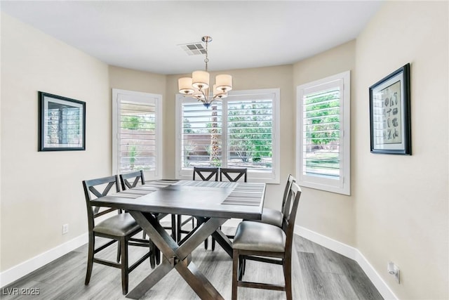 dining space with visible vents, baseboards, wood finished floors, and a notable chandelier
