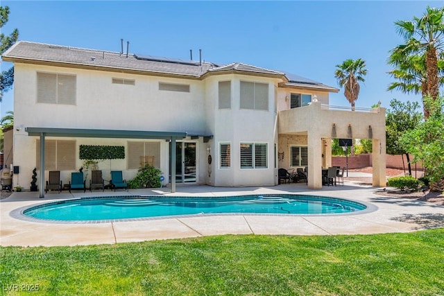 rear view of property with roof mounted solar panels, fence, an outdoor pool, and a patio area