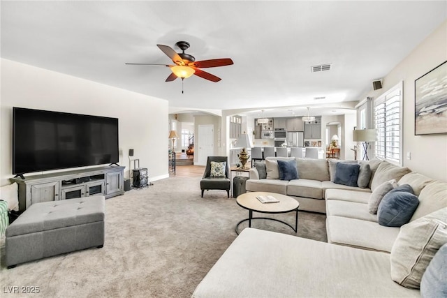 carpeted living room featuring arched walkways, ceiling fan, visible vents, and plenty of natural light