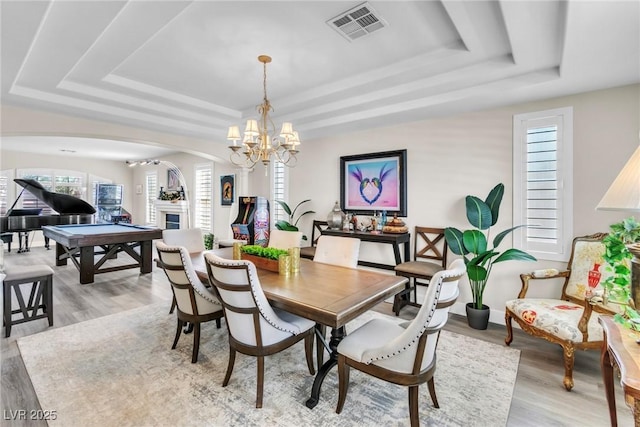 dining space featuring visible vents, light wood-type flooring, a tray ceiling, arched walkways, and a notable chandelier