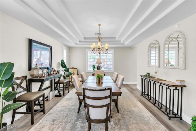 dining space featuring light wood-type flooring, baseboards, a tray ceiling, and an inviting chandelier