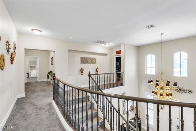 corridor with carpet flooring, a notable chandelier, baseboards, an upstairs landing, and visible vents