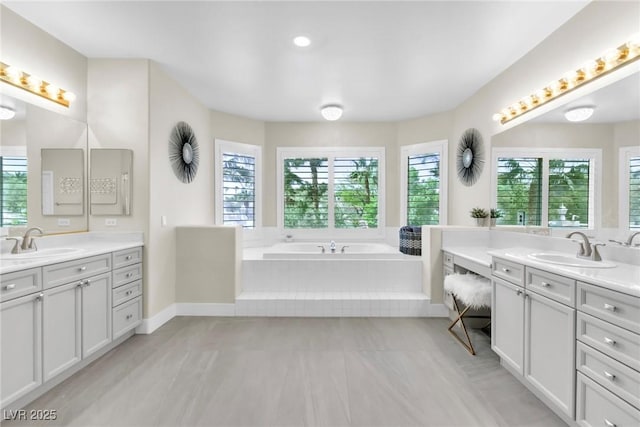 full bath featuring two vanities, a sink, and a bath