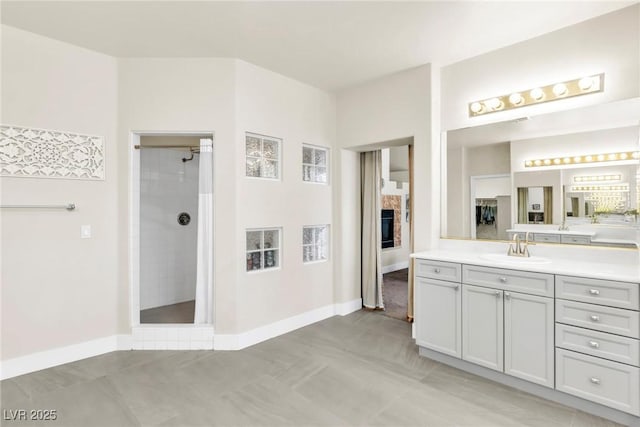 bathroom with vanity, baseboards, a fireplace, and tiled shower