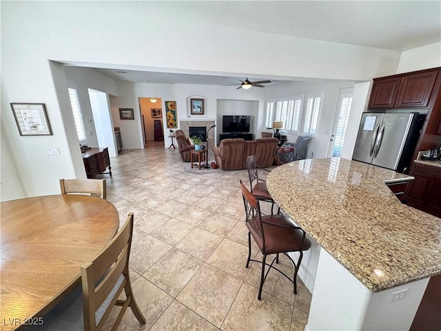 kitchen with ceiling fan, light stone counters, a center island, freestanding refrigerator, and a kitchen bar