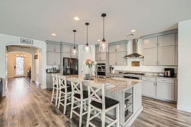 kitchen with a breakfast bar, wall chimney exhaust hood, arched walkways, gray cabinetry, and stainless steel appliances