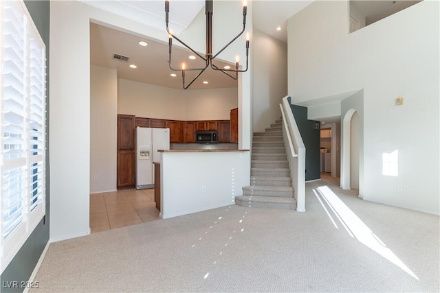 unfurnished living room with plenty of natural light, a high ceiling, visible vents, and light colored carpet