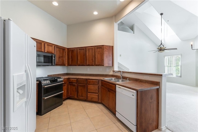kitchen featuring dark countertops, a sink, white appliances, a peninsula, and a ceiling fan