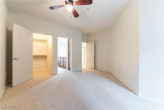 unfurnished bedroom featuring a walk in closet, baseboards, light carpet, and a closet