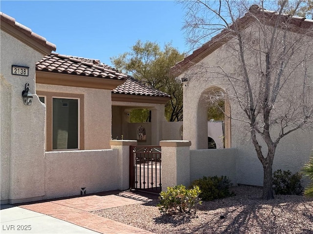 exterior space with a gate, stucco siding, a tile roof, and fence