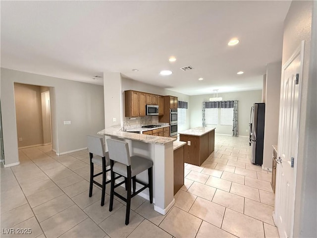 kitchen featuring light tile patterned flooring, appliances with stainless steel finishes, a center island, a peninsula, and visible vents