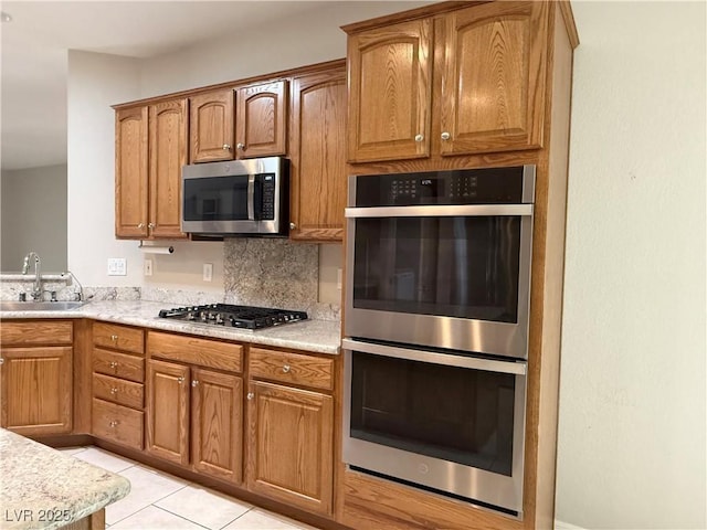 kitchen with light countertops, a sink, brown cabinetry, and stainless steel appliances