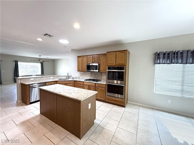 kitchen with light stone countertops, appliances with stainless steel finishes, brown cabinetry, a peninsula, and visible vents