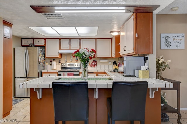 611 Spyglass Ln, Las Vegas, NV 89107 - kitchen with a peninsula, light tile patterned floors, stainless steel appliances, and tile countertops