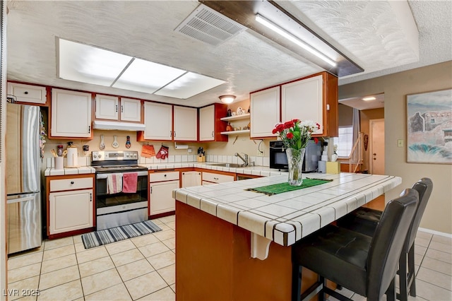 611 Spyglass Ln, Las Vegas, NV 89107 - kitchen featuring tile countertops, visible vents, appliances with stainless steel finishes, a peninsula, and light tile patterned flooring