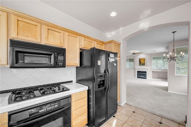 kitchen featuring tile countertops, light colored carpet, arched walkways, black appliances, and light brown cabinets
