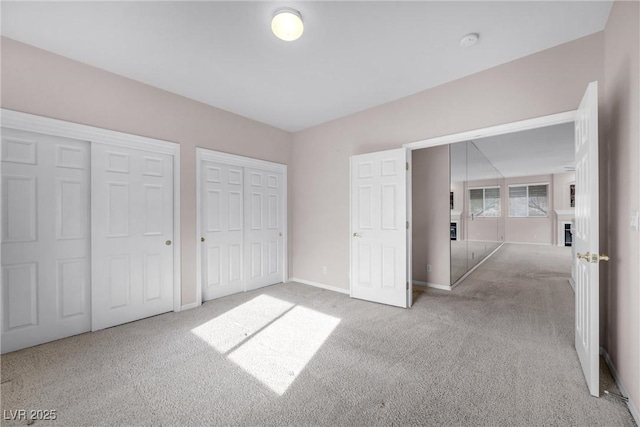 unfurnished bedroom featuring light colored carpet, baseboards, and multiple closets