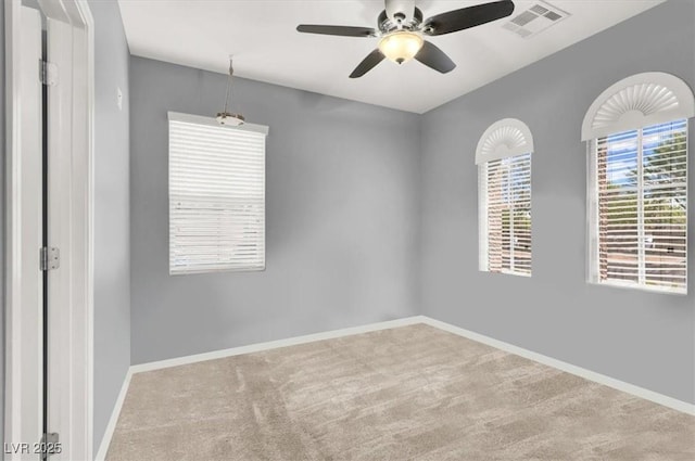 carpeted spare room with visible vents, baseboards, and ceiling fan